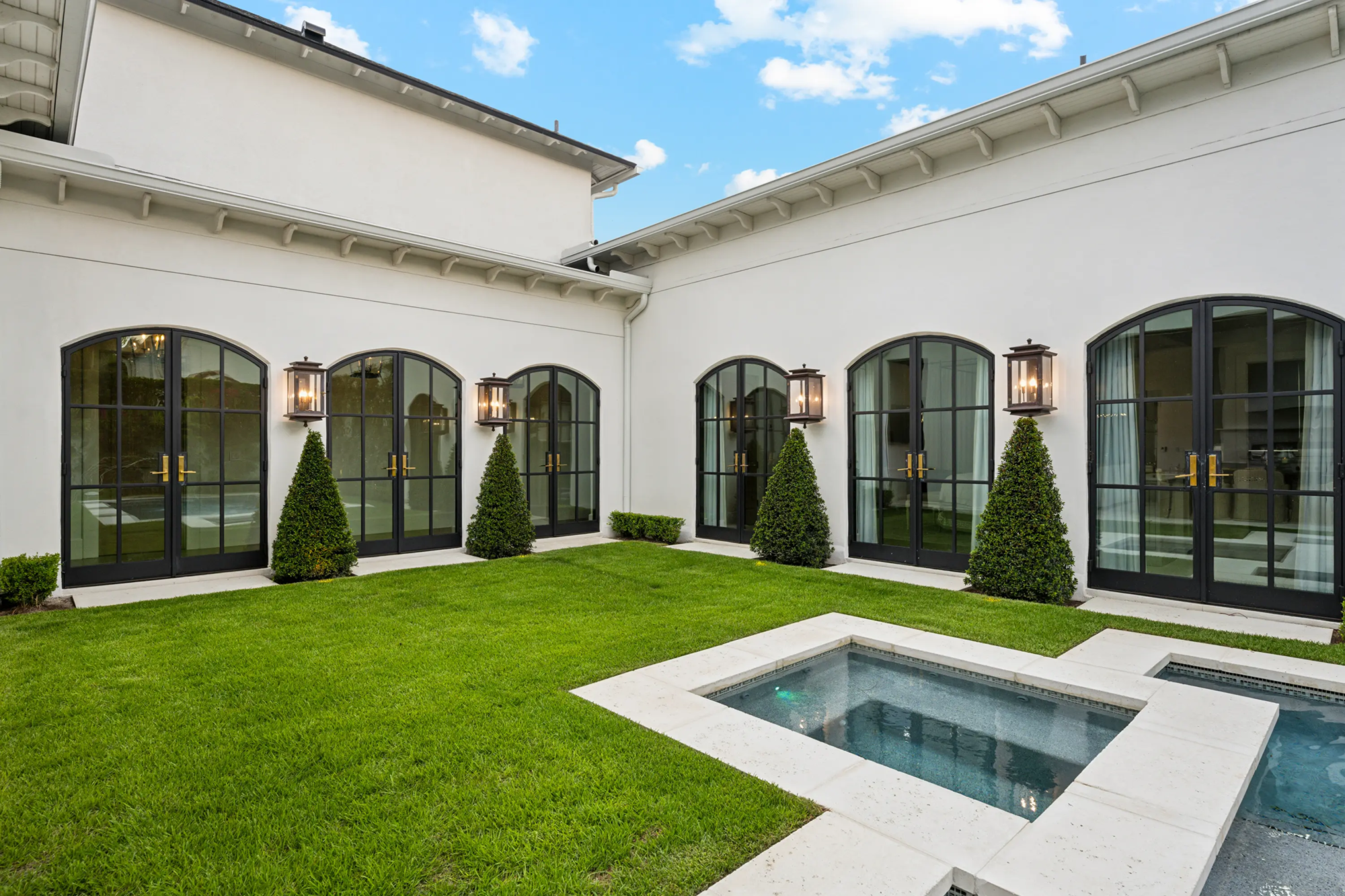 Interior courtyard lawn lined with a row of matching conical topiaries set against arched doorways, showing consistent hedge and topiary spacing.